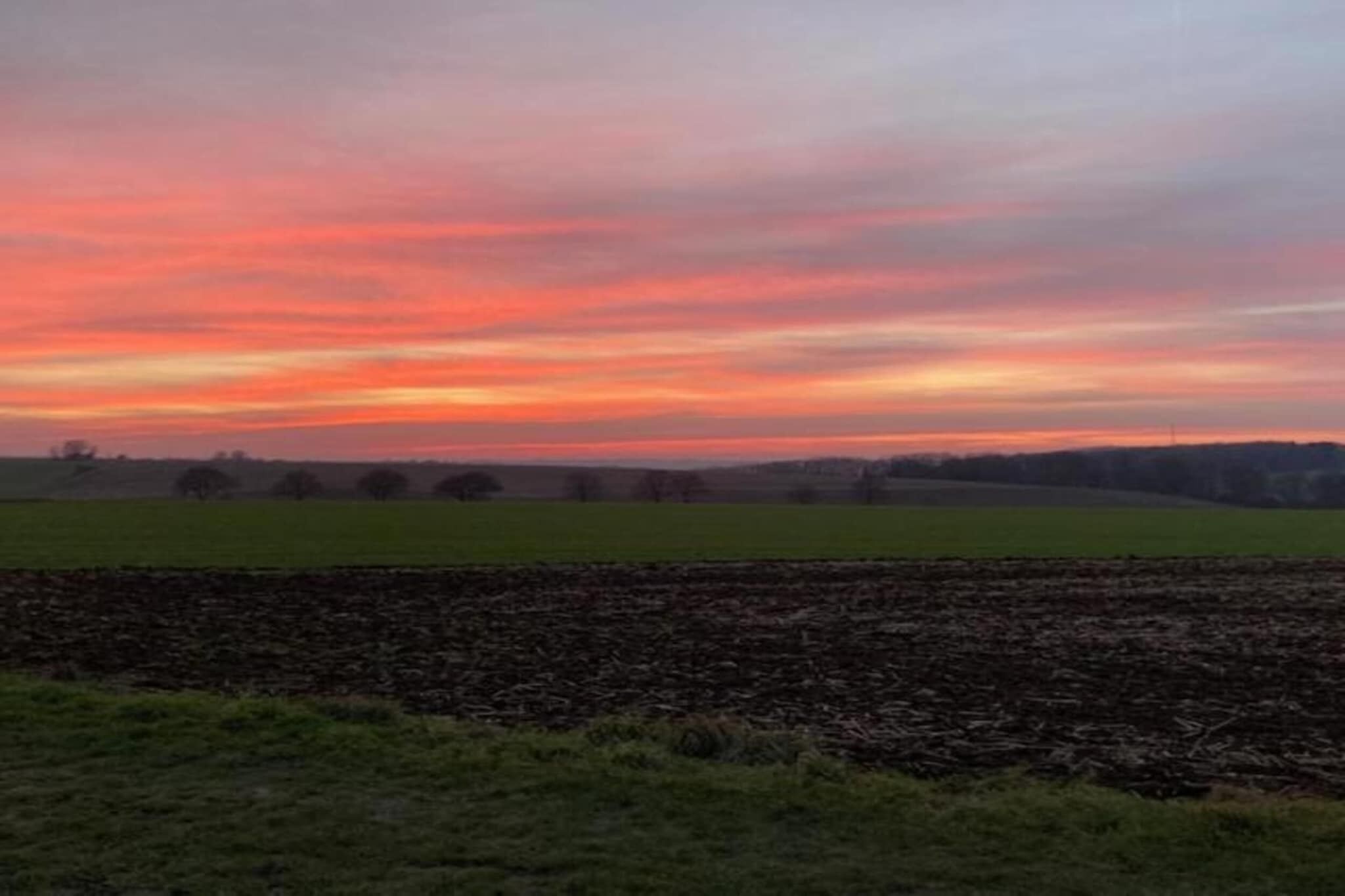 A rural landscape with fields and a sunset sky.