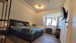 A bedroom with a bed, a desk, a chair, a TV mounted on the wall, and a window with curtains.