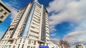 Ein hohes, modernes Gebäude mit einer geschwungenen Glasfassade und einem blauen Schild, das auf eine allgemeine Versicherungsgesellschaft hinweist.
