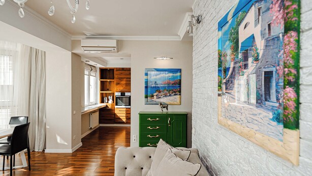 Ein modernes Wohnzimmer mit einer Couch, einem Esstisch und einem grünen Schrank. An der Wand hängt ein Bild und es gibt ein Fenster mit Vorhängen.