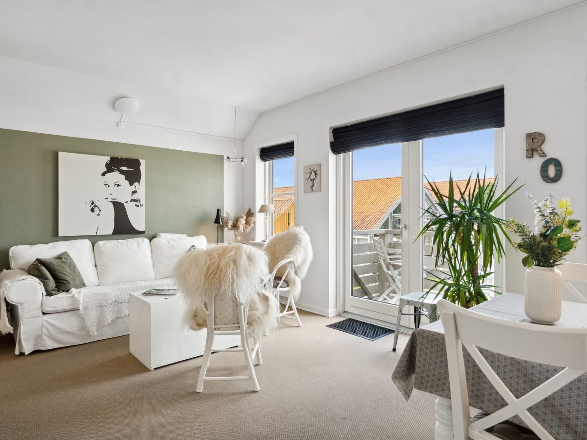 Un salon moderne avec un canapé blanc, une table à manger avec des chaises et une grande fenêtre donnant sur l’extérieur.