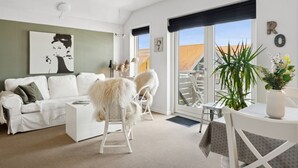 Een moderne woonkamer met een witte bank, een eettafel met stoelen en een groot raam met uitzicht.