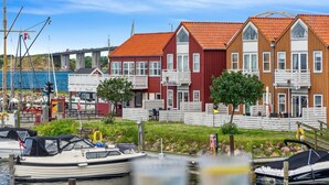 Een jachthaven met aangemeerde boten, een rij kleurrijke huizen en een brug op de achtergrond.