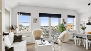 Een ruime woonkamer met een witte bank, een eettafel en uitzicht op een jachthaven door grote ramen.