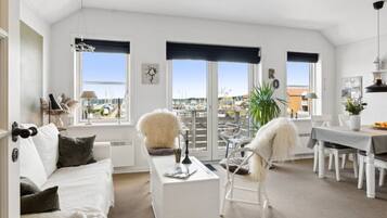 Un salon spacieux avec un canapé blanc, une table à manger et une vue sur une marina, visible à travers de grandes fenêtres.
