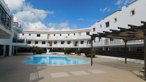 A courtyard with a swimming pool, white buildings, and a pergola. - Paramount Gardens Resorts C202 (Tersefanou)