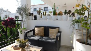 A balcony with a wicker sofa, a table with a pitcher, and various potted plants. - Paramount Gardens Resorts C202 (Tersefanou)