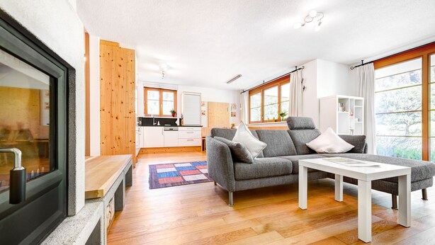 A modern living room with a sofa, coffee table, and a view of the kitchen and dining area.