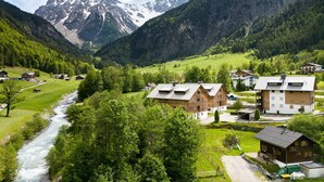 Een bergdorp met traditionele huizen, een rivier en besneeuwde toppen op de achtergrond.