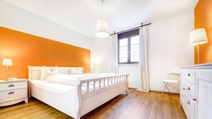 A bedroom with a white bed, wooden flooring, and orange walls.