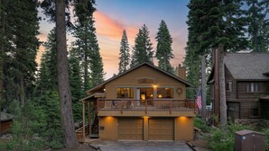 A two-story log cabin with a balcony, surrounded by tall trees and a sunset sky. - Wildwood by AvantStay | Hot Tub, 5mins to Lake (Tahoe Vista)
