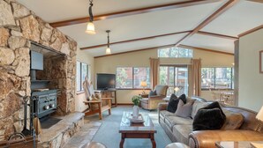 A cozy living room with stone walls, a fireplace, leather furniture, and large windows. - Wildwood by AvantStay | Hot Tub, 5mins to Lake (Tahoe Vista)