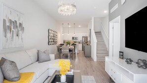 En moderne stue med sofa, sofabord og fjernsyn på et stativ. Der er en trappe, der fører op til en etage.