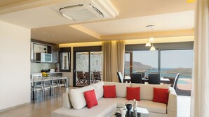 Sala de estar moderna com um sofá branco, almofadas vermelhas, uma mesa de centro de vidro e vista para o mar através de grandes janelas.