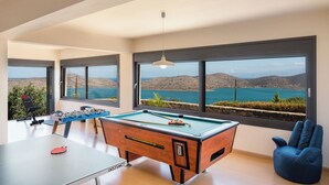 Mesa de bilhar com mesa de futebol de mesa e mesa de tênis em um salão com grandes janelas com vista para uma paisagem deslumbrante.