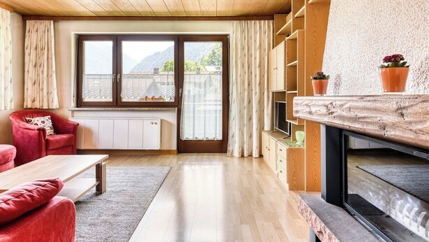 A modern living room with a wooden ceiling, a red sofa, a wooden coffee table, a television, and a large window with a view of mountains. - Apartment Sassella - Mäser-Apartments (Tschagguns)