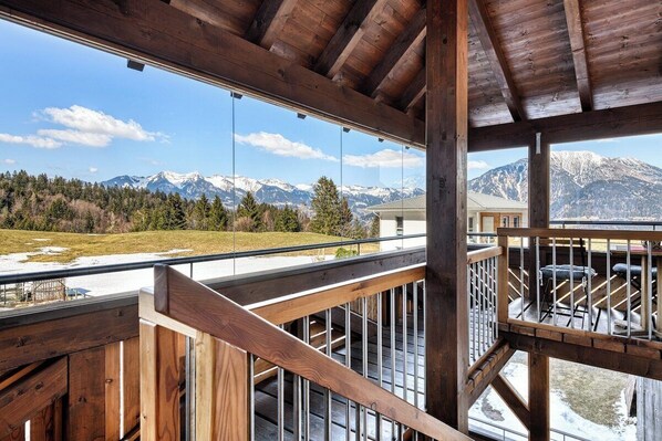 A wooden balcony with a view of snow-capped mountains and a clear sky.