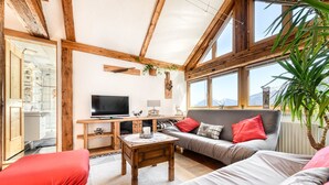 A cozy living room with a TV, wooden furniture, and large windows offering a mountain view. - Chalet Fischer (Bürserberg)