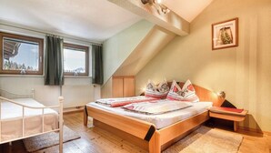 A bedroom with a wooden bed, a white bedside table, a nightstand, a window with curtains, and a framed picture on the wall. - Chalet Fischer (Bürserberg)