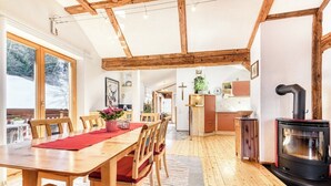 A cozy, well-lit wooden interior with a dining area, kitchen, and a wood-burning stove. - Chalet Fischer (Bürserberg)