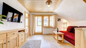 A cozy room with wooden floors, a red sofa, a wooden cabinet, and a large window with curtains. - Appartement Zentral de Luxe (Brand)