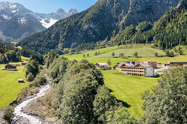 A mountain village with a river, houses, and a large building with a sloped roof. - Brandnerhus Nr. 02 - Garten 3-Zimmer Ferienwohnung (Brand)