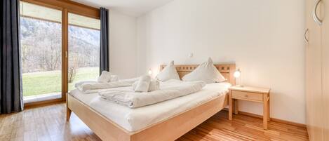 A bedroom with a wooden bed, a nightstand, and a large window with curtains.