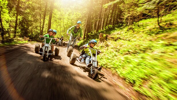 Un chemin de terre bordé d’arbres, sur lequel circulent trois personnes à bord de quads.