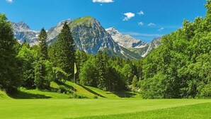 A lush green landscape with a golf course, a flag, and mountains in the background.