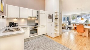 A modern kitchen with white cabinets, a built-in oven, and a dining area with a wooden table and orange chairs.