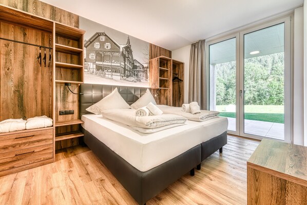Une chambre moderne avec un grand lit, des meubles de rangement en bois et une fresque représentant un bâtiment.