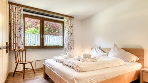 A bedroom with a wooden bed, a chair, a window with curtains, and a radiator.