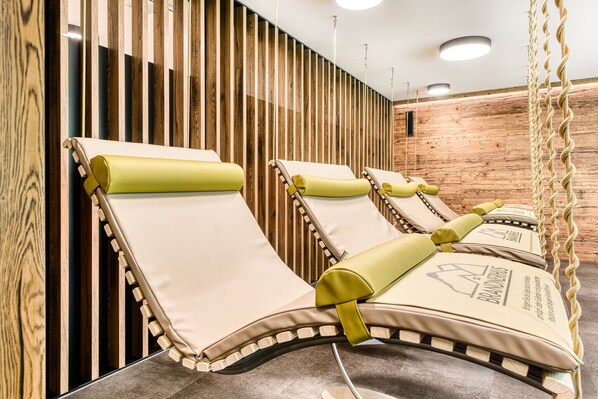 A row of sun loungers with green cushions and a logo, against a wooden wall with vertical slats.