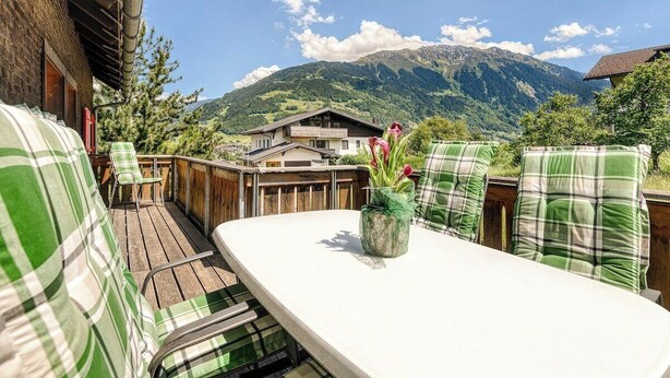A wooden deck with a white table and green plaid chairs, overlooking a mountain. - Chalet Mariedl (Tschagguns)