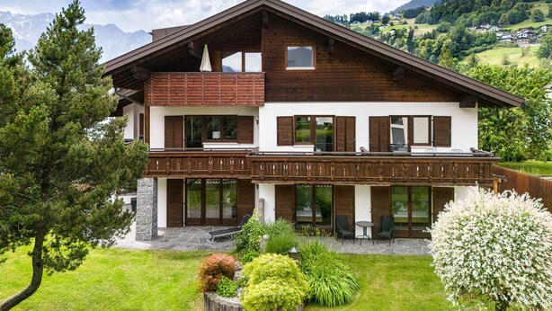 Eine zweistöckige Chalet mit Balkon, Stein Fundament und Blick auf eine Berglandschaft.