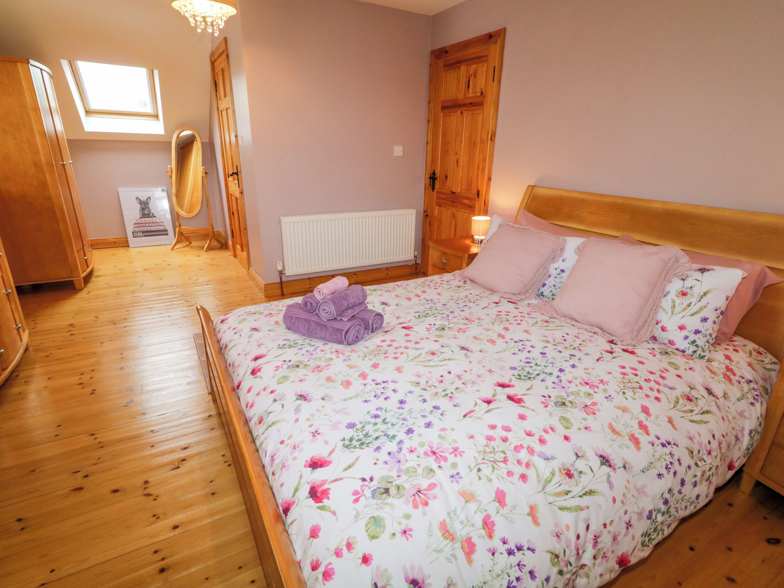 A bedroom with a wooden floor, a bed with floral bedding, a radiator, and a wooden wardrobe.