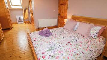 A bedroom with a wooden floor, a bed with floral bedding, a radiator, and a wooden wardrobe.