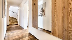 A hallway with wooden flooring, a staircase, and a wall-mounted mirror. - Alpenblick Appartements - 5-Zimmer Gardenapartment (Schruns)