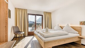 A modern bedroom with a wooden bed, a chair, and a view of a mountainous landscape through a large window. - Alpenblick Appartements - 5-Zimmer Gardenapartment (Schruns)