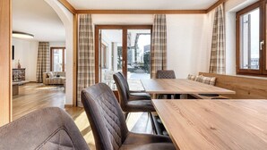 A dining area with a wooden table and leather chairs, a sofa, and a view through glass doors. - Alpenblick Appartements - 5-Zimmer Gardenapartment (Schruns)