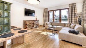 A modern living room with a wooden dining table, a sofa, and a TV mounted on the wall. - Alpenblick Appartements - 5-Zimmer Gardenapartment (Schruns)