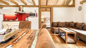 A cozy living area with a wooden ceiling, a red kitchen in the background, and a brown sofa with cushions.