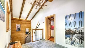 A wooden staircase with a metal railing, a chandelier, and a wall-mounted picture of a snowy landscape.