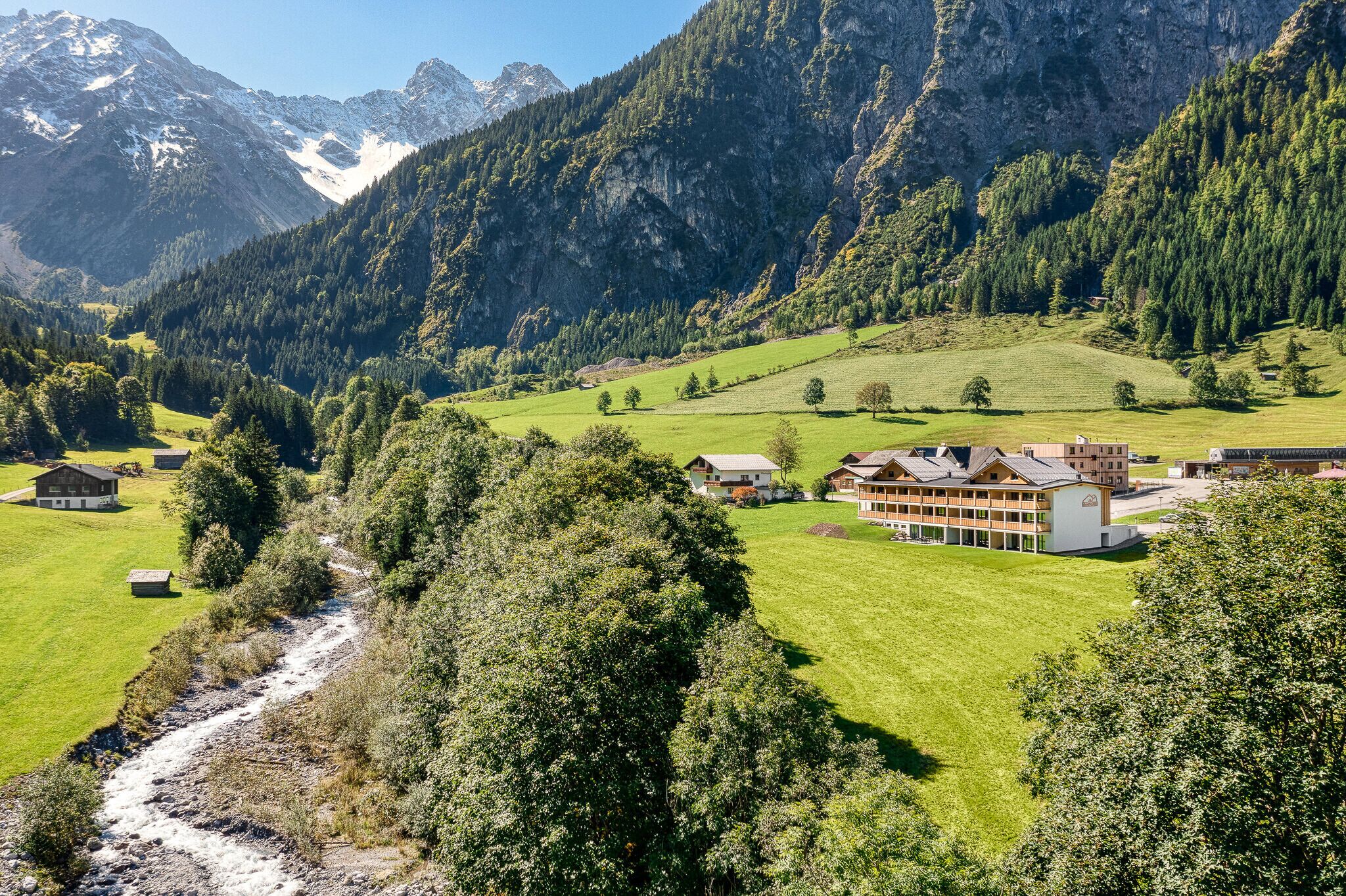 A mountain village with a river, houses, and a large building with a sloped roof.