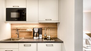 A modern kitchen with a built-in microwave, coffee maker, and utensils hanging on the wall. - Alpenblick Appartements - Studio (Schruns)