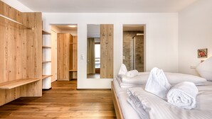 A hotel room with wooden flooring, a bed with white linens, a wooden wardrobe, and a shower area. - Alpenblick Appartements - Studio (Schruns)