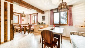 A cozy kitchen with wooden beams, a dining area with a table and chairs, and a window with curtains.