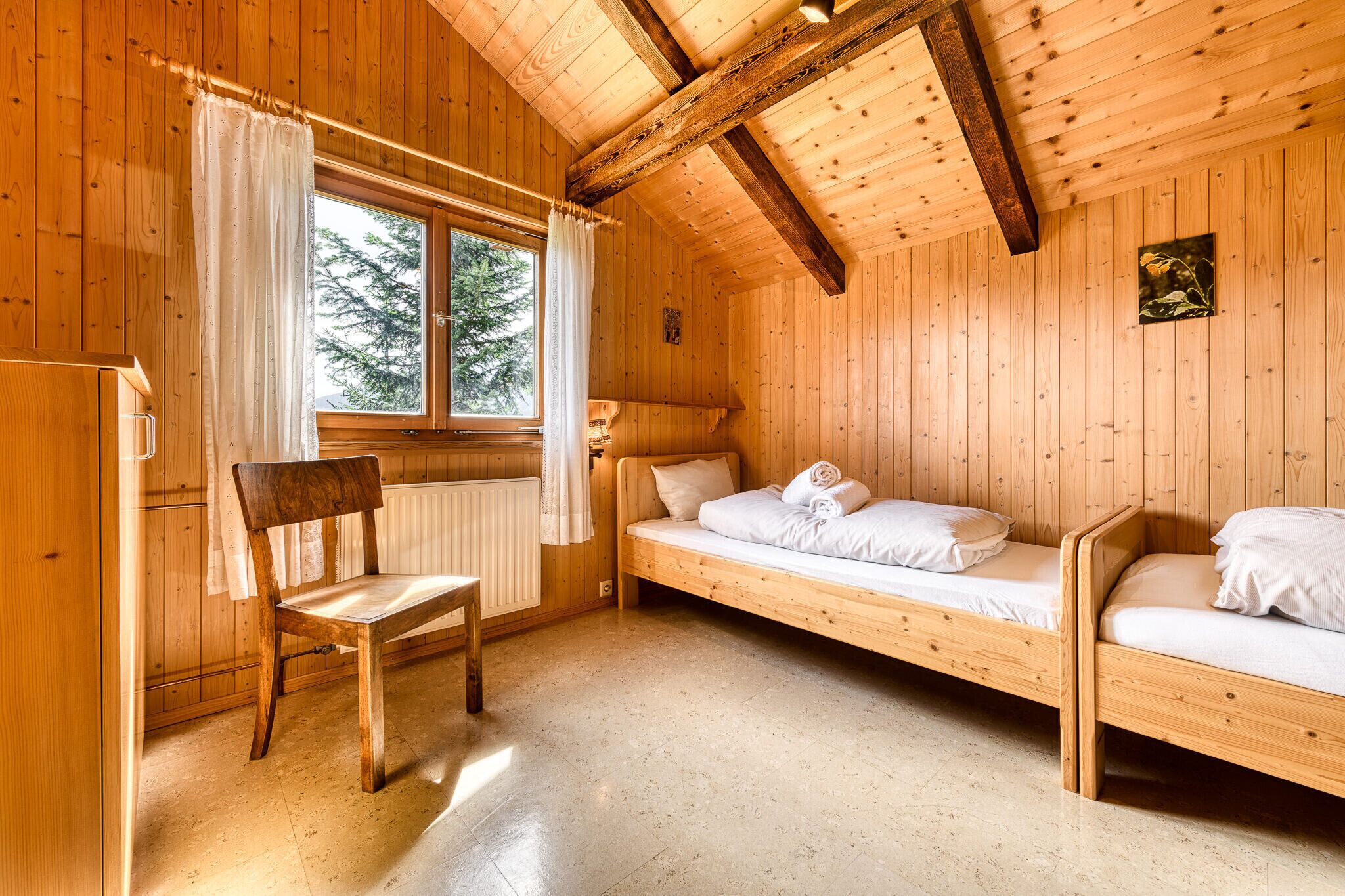 Une pièce de cabane en bois comprenant deux lits superposés, une chaise en bois, une fenêtre avec des rideaux et un radiateur.
