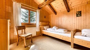 Une pièce de cabane en bois comprenant deux lits superposés, une chaise en bois, une fenêtre avec des rideaux et un radiateur.