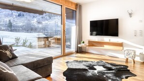 Ein modernes Wohnzimmer mit einer großen Schiebeglasdoor zum Balkon, einem an der Wand befestigten Flachbildfernseher und einem rustikalen Teppich auf dem Boden.